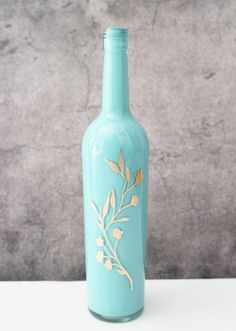 a blue bottle with gold leaves painted on the side sitting on a white table next to a gray wall