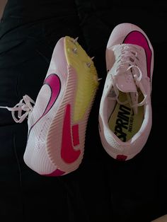 two pairs of pink and yellow nike shoes on a black surface with white laces