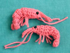 two pink crocheted lobsters with black eyes on a green surface, one in the shape of a squid