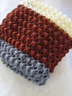 four different colors of crocheted blanket laying on top of a white furnishing