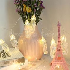 a vase with flowers and fairy lights in front of the eiffel tower