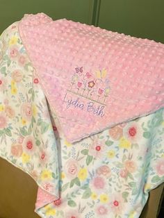 a pink blanket with an embroidered name and flowers on it sitting on a wooden chair