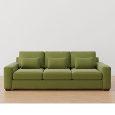 a green couch sitting on top of a hard wood floor next to a white wall