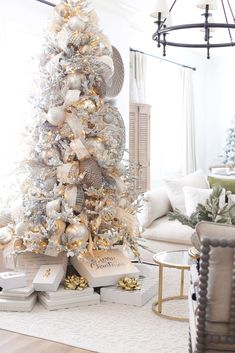 a white christmas tree decorated with gold and silver ornaments in a neutral living room setting