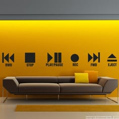 a couch sitting in front of a yellow wall with various signs on the wall behind it