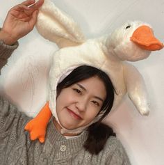 a woman wearing a white duck hat with an orange beak on her head and hands behind her head