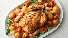 a chicken and potatoes on a plate with rosemary garnish, sitting on a white surface