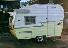 an old camper parked in front of a house with the sun shining on it