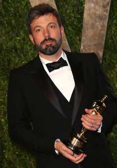 a man in a tuxedo holding an award for best performance by an actor