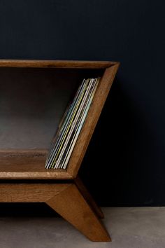 a wooden shelf with various records in it on the floor next to a black wall