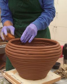 a person in purple gloves working on a clay pot