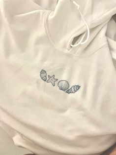 a white sweatshirt with shells and starfish embroidered on the front, sitting on a bed