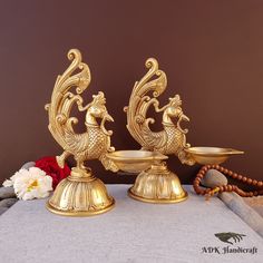 two golden candlesticks sitting next to each other on a white cloth with flowers