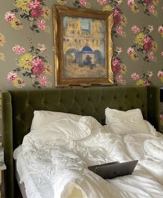 a laptop computer sitting on top of a bed in front of a floral wallpaper