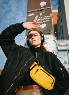 a woman wearing headphones and carrying a yellow bag in front of a tall building