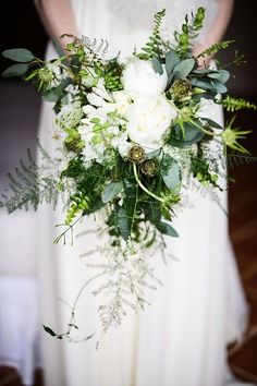 a bridal holding a bouquet of white flowers and greenery in her hands,