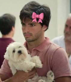 a man holding a small white dog wearing a pink bow