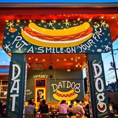 the entrance to a hot dog shop with people sitting at tables under lights and signs