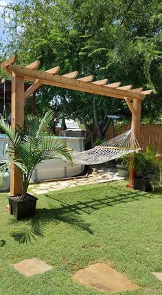 an outdoor hammock in the middle of a yard with a tree and potted plant