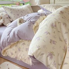 a bed with purple and white comforters, pillows and stuffed animals on the pillowcase