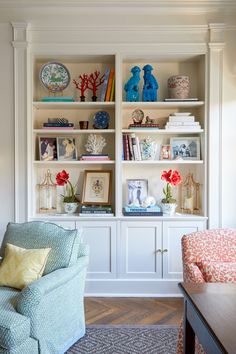 a blue chair sitting in front of a white book shelf filled with books and vases