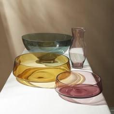 three different colored glass bowls sitting on top of a white table next to a vase