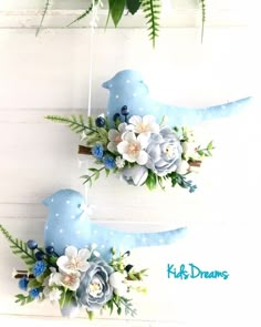 two blue birds decorated with flowers and greenery hanging from strings on a white wall