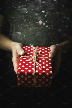 a person holding a red gift box with white polka dots and a string tied around it