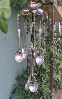 a chandelier with spoons hanging from it's sides and green plants in the background