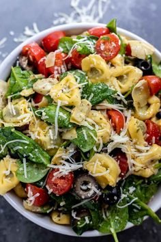 a white bowl filled with pasta salad topped with spinach, tomatoes, mushrooms and parmesan cheese