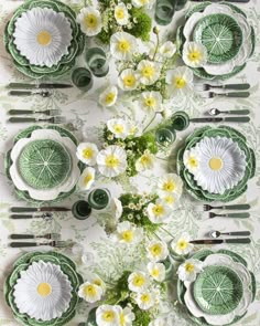 the table is set with green and white plates, silverware, and flower arrangements