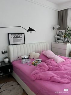 a bed with pink sheets and pillows in a bedroom next to a wall mounted poster