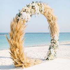 a wedding arch on the beach with flowers and pamodia in front of it