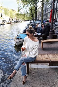 a woman sitting on a bench next to a body of water