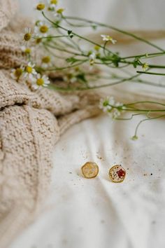 two small gold buttons sitting on top of a bed next to some wildflowers