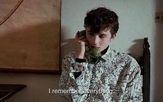 a young man is talking on the phone and holding an apple in his hand while sitting down