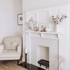 An elegant, white staggered tile fireplace with white trim is fitted with a white mantel in this living room. The mantel is decorated with white and gold decor arranged next to cotton branches in a white jug vase. A beige corner chair with black wood legs is seated next to the fireplace...   Image: the_artist_home