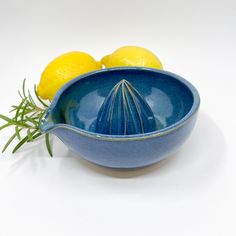 a blue bowl with a whisk in it next to two lemons on a white background