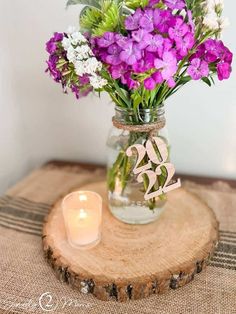 a vase filled with purple flowers sitting on top of a wooden table next to a candle