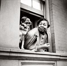 a black and white photo of a woman sitting on a window sill with her dog