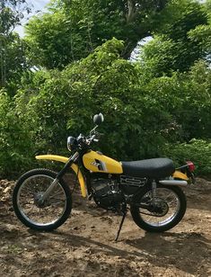 a yellow dirt bike parked on top of a dirt field next to some green trees