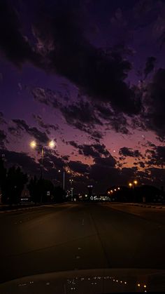 the night sky is lit up with street lights and clouds in the distance as seen from an empty parking lot