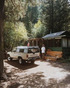 a man standing next to a white van in front of a forest house with trees