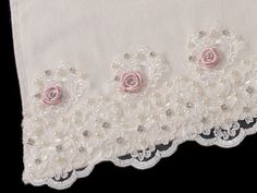 two pink roses are on the edge of a white cloth with beaded trims