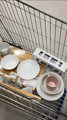 a shopping cart filled with plates and bowls sitting on top of a wooden table next to a microwave