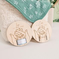 two wooden coasters with pictures of hands on them, one holding a baby's hand