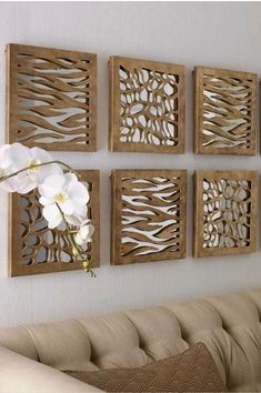 four wooden wall art pieces hanging on the wall next to a couch with flowers in it