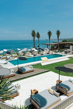 an aerial view of the pool and lawn area at a resort by the ocean with lounge chairs, umbrellas and palm trees