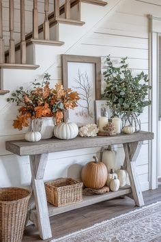 a wooden table topped with lots of pumpkins next to a stair case filled with greenery