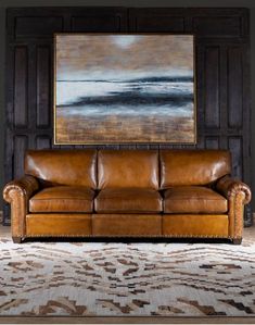 a brown leather couch sitting in front of a painting